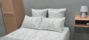 Una cama con una colcha estampada y almohadas, un armario de madera y una mesita de noche con una lámpara.