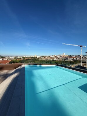 A rooftop swimming pool with a clear view of a cityscape and a construction crane in the background.