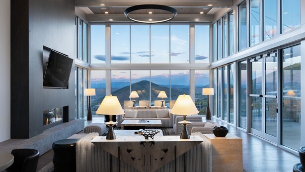 Een moderne woonkamer met een open haard, grote ramen en uitzicht op bergen.