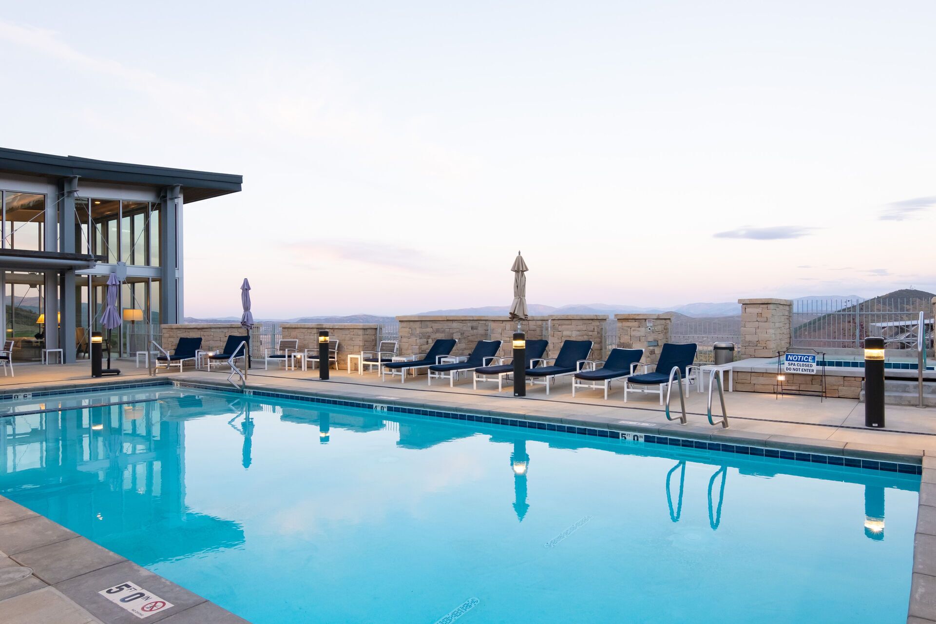 A pool with lounge chairs, a spa sign, and a view of mountains.