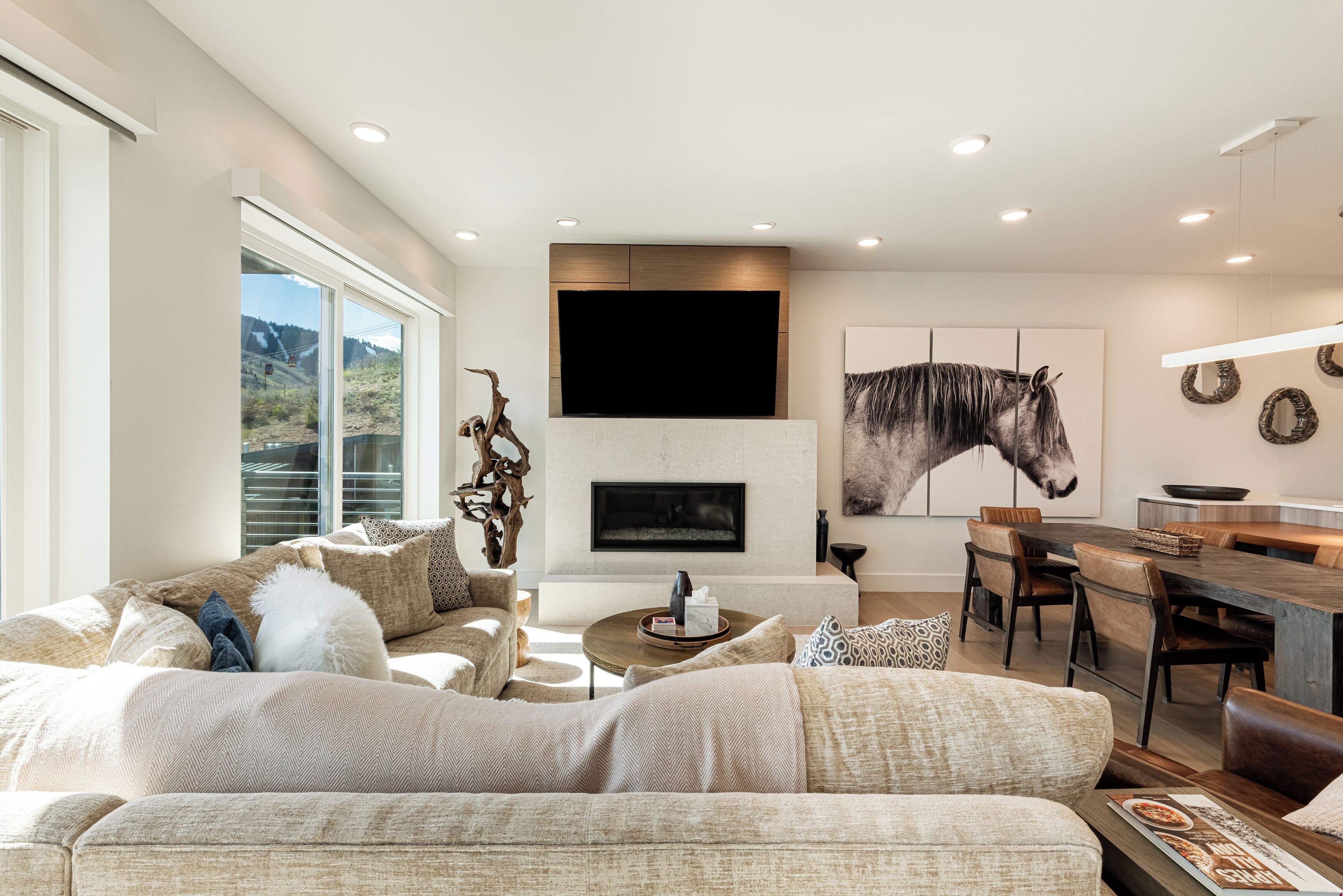 A modern living room with a fireplace, a large horse painting, and a dining area with a wooden table and chairs.