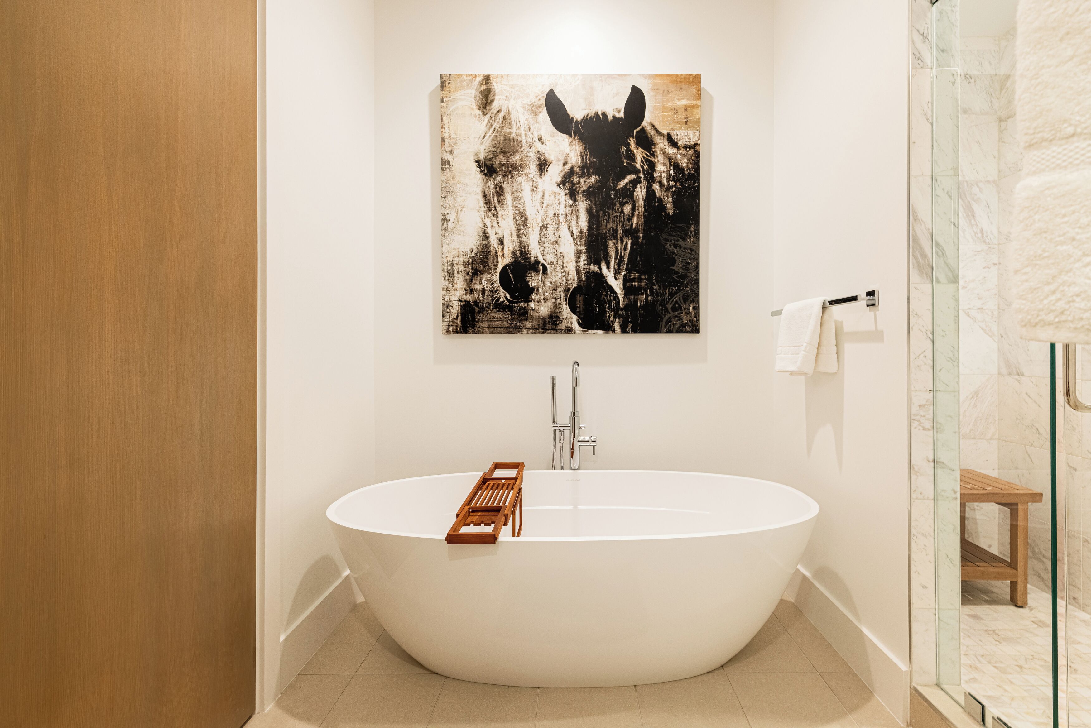 Ein modernes Badezimmer mit freistehender Badewanne, einer Holzbadematte, einem Handtuchhalter und einer Duschkabine aus Glas.