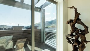 Een kamer met een groot raam, een houten sculptuur en uitzicht op een bergachtig landschap.