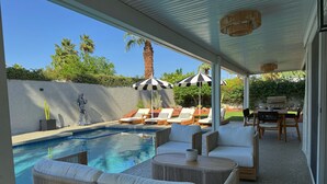 Un espacio al aire libre techado con piscina, sillones de descanso y una zona de barbacoa.
