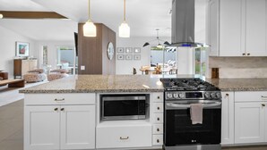 Una cocina moderna con armarios blancos, microondas integrado, estufa a gas e iluminación colgante.