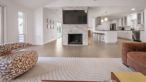 Un amplio salón con chimenea, muebles modernos y una cocina al fondo.