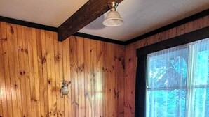 Een slaapkamer met houten wanden, een bed, een nachtkastje, een lamp en een raam met uitzicht op bomen.