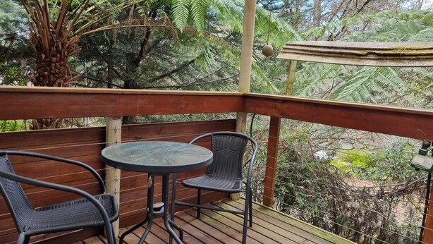 Een houten terras met een ronde tafel en twee stoelen, omgeven door weelderig groen en bomen.