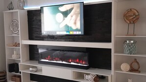 Ein modernes Wohnzimmer mit Flachbildfernseher über einem Kamin, umgeben von weißen Regalen mit Dekorationselementen.