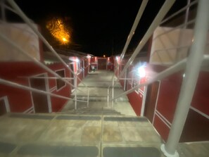 Una escalera conduce a un nivel superior, rodeada de paredes rojas y barandillas blancas, con una fuente de luz al fondo.