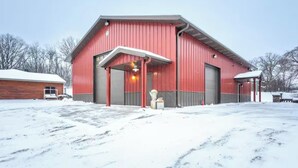 A red barn with a covered entrance, a wooden building to the left, and snow on the ground.