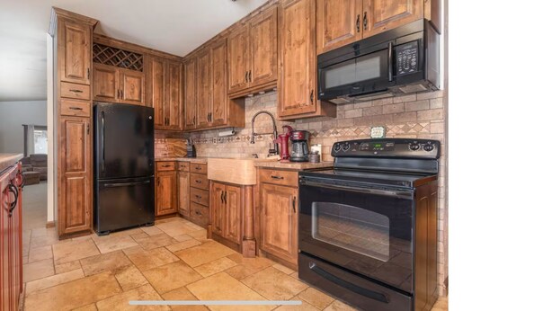 A kitchen with wooden cabinets, a black refrigerator, a microwave, a coffee maker, and a stove.