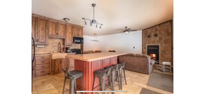 A kitchen with wooden cabinets, a central island with stools, a microwave, and a fireplace. - Private 40-Acre Cabin + Indoor Pickleball & Trails (Sauk Centre)