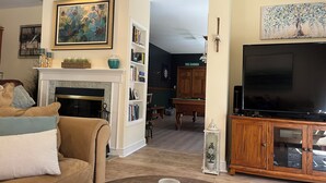 Una sala de estar con chimenea, televisor, estantería y mesa de billar.