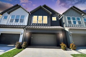 Ein modernes, zweistöckiges Haus mit Garage, überdachter Auffahrt und kleinen Sträuchern.