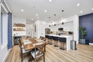 Eine moderne Küche mit weißen Schränken, einer zentralen Kochinsel mit Barhocker, einem Kühlschrank und einer Mikrowelle.