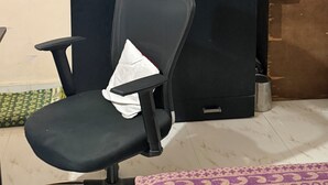 Une pièce comprenant un bureau avec un fauteuil noir, une armoire et une étagère avec des vêtements pliés.