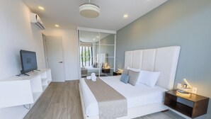 Quarto de hotel moderno com cama, mesas de cabeceira, televisão e uma janela grande.
