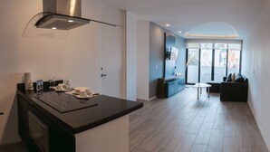 Uma cozinha moderna com uma ilha central, uma sala de jantar com mesa e cadeiras, e uma sala de estar com sofá e televisão.