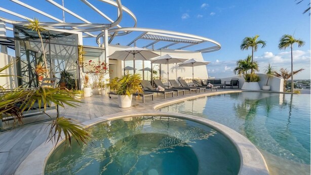 Piscina infinita moderna com espreguiçadeiras e guarda-sóis, cercada por plantas em vasos e uma estrutura arquitetônica singular.