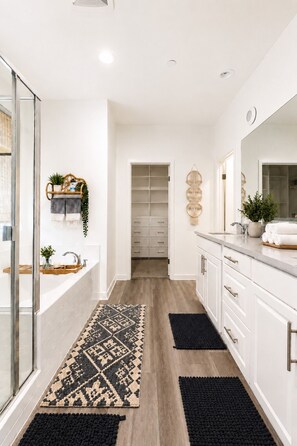 A modern bathroom with a glass shower enclosure, a white vanity with a large mirror, and a wooden floor.