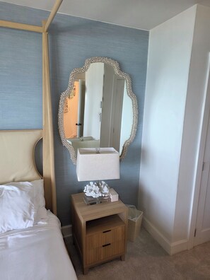 A hotel room with a bed, a bedside table with a lamp, a mirror with a decorative frame, and a wardrobe.