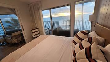 Habitación de hotel con una cama grande, vista al océano, un balcón con una silla y un ventilador de techo.