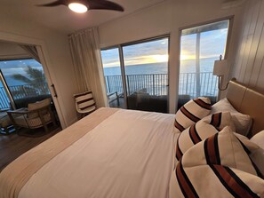 Habitación de hotel con una cama grande, vista al océano, un balcón con una silla y un ventilador de techo.