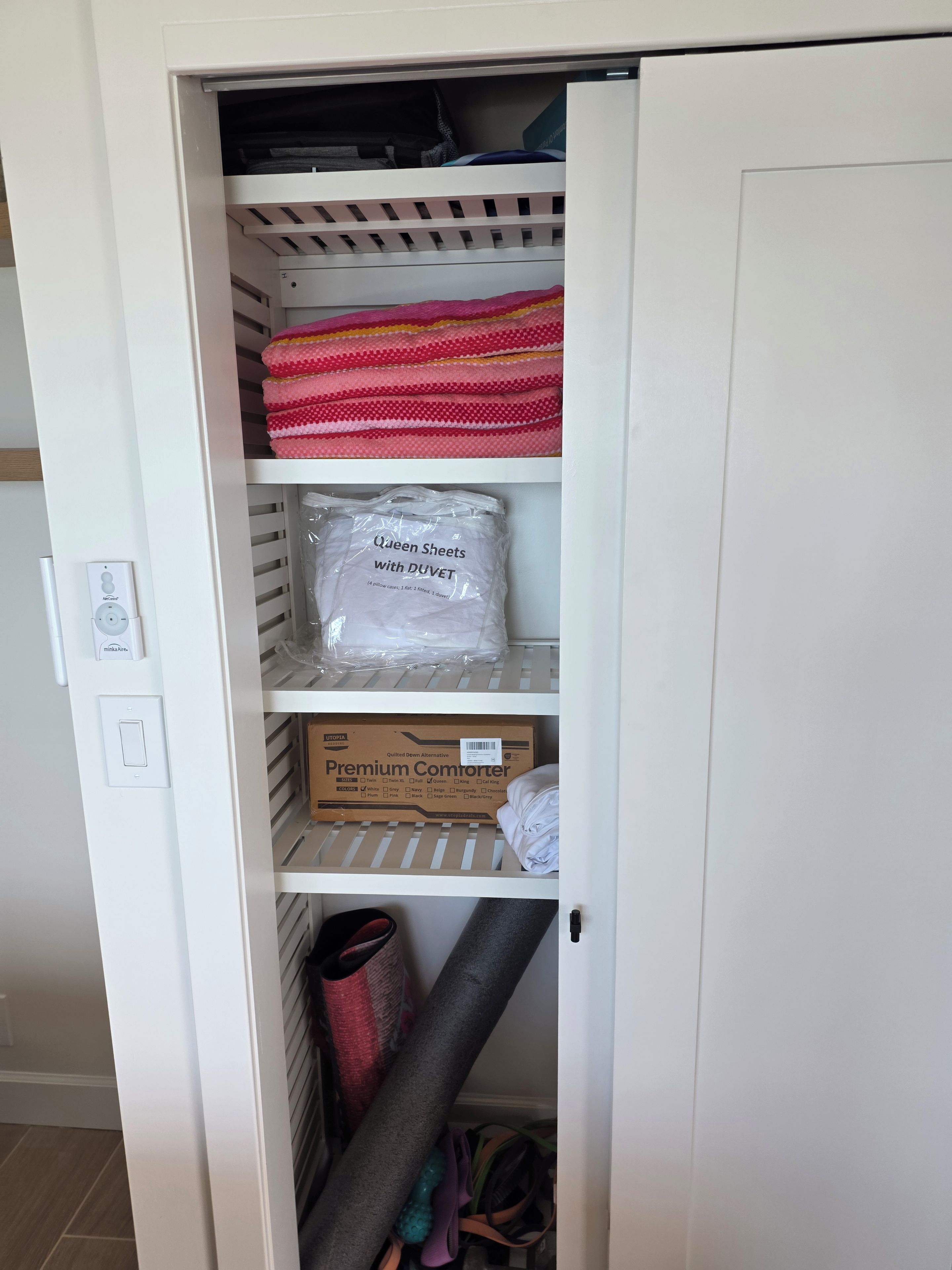 Un depósito con estantes que contienen mantas dobladas, un paquete etiquetado 'Sábanas Queen con DUVET' y una caja etiquetada 'Edredón Premium'.