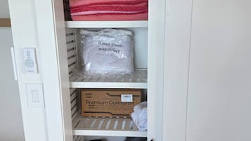 Un depósito con estantes que contienen mantas dobladas, un paquete etiquetado 'Sábanas Queen con DUVET' y una caja etiquetada 'Edredón Premium'.