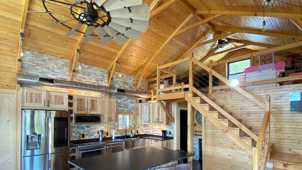 Una cocina amplia con una isla central, vigas de madera en el techo e una escalera empotrada.