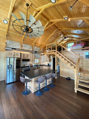 A spacious kitchen with a central island, wooden ceiling beams, and a built-in staircase.