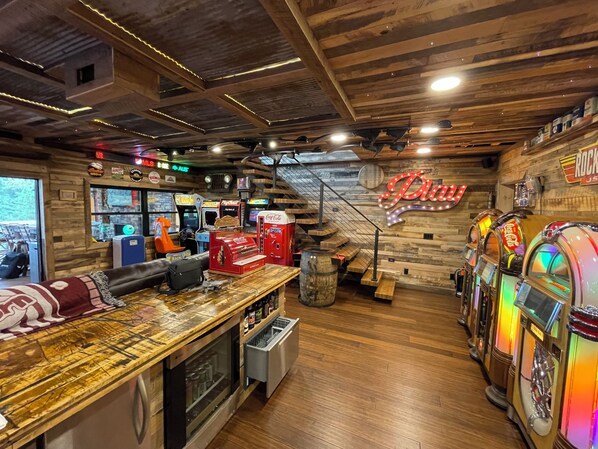 A retro-themed bar area with arcade machines, a neon sign, and a wooden interior.