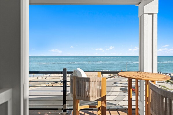 A balcony with a view of the ocean, a wooden chair, and a small round table.