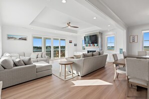 A spacious living area with a large sofa, a dining table, and a TV mounted on the wall.