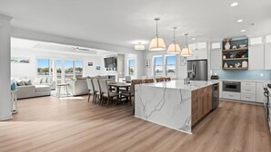 Cozinha moderna com ilha de mármore, piso de madeira e iluminação pendente.