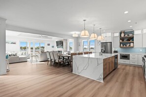 A modern kitchen with a marble island, wooden flooring, and pendant lighting.
