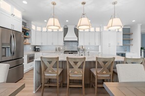 A modern kitchen with white cabinets, a central island with bar stools, stainless steel appliances, and pendant lighting.