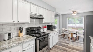 A modern kitchen with white cabinets, a stove, microwave, and a dining area with a table and chairs. - Game Room & BBQ at Renovated Montgomery Retreat (Montgomery)