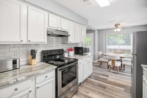 Una cocina moderna con armarios blancos, estufa, microondas y un comedor con mesa y sillas.