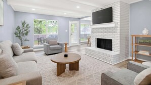 A living room with a fireplace, sofa, coffee table, and a television mounted on the wall. - Game Room & BBQ at Renovated Montgomery Retreat (Montgomery)