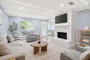 Una sala de estar con chimenea, sofá, mesa de centro y televisor montado en la pared.