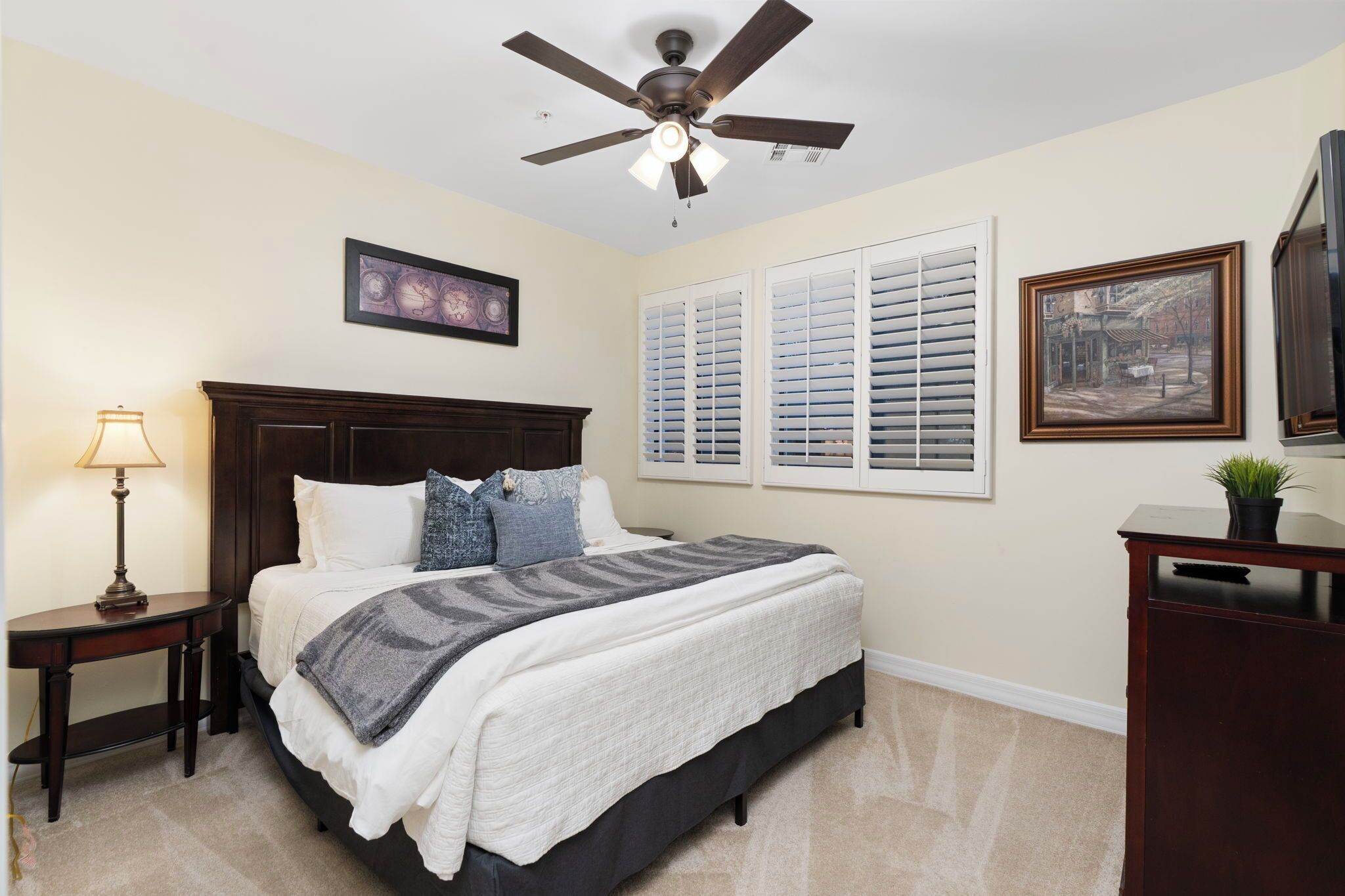 A bedroom with a bed, a nightstand, a lamp, a ceiling fan, and a painting on the wall.