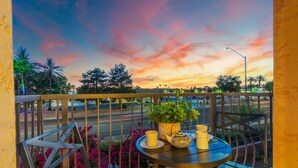 A balcony with a table set for two, featuring a potted plant and yellow cups.