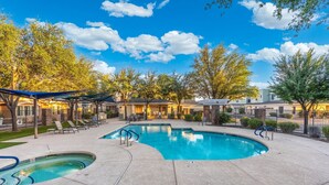 A swimming pool with a sunken hot tub, lounge chairs, and a covered patio area.