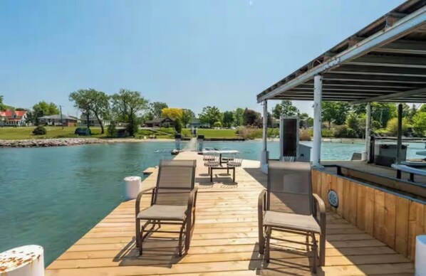 A wooden deck with lounge chairs and a covered area overlooking a body of water.