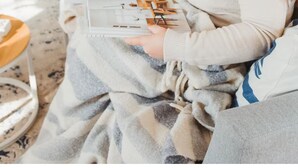 Una persona sentada en un sofá con un cuaderno y una taza, en una habitación con chimenea y una puerta al fondo.