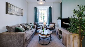 Ein Wohnzimmer mit einer Couch, Sesseln, einem Couchtisch, einem Fernseher und einer Pflanze.