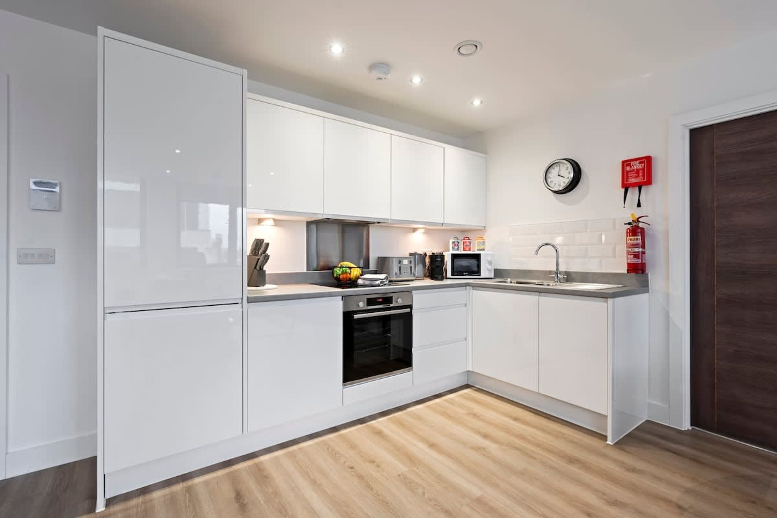 Une cuisine moderne avec des meubles blancs, un four à micro-ondes, un évier et une horloge au mur.