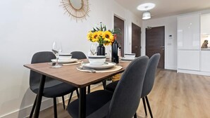 A dining area with a wooden table, black chairs, a vase with sunflowers, and a wine bottle. - Pristine Flat Ideal for Small Groups Sleeps 4 (Manchester)